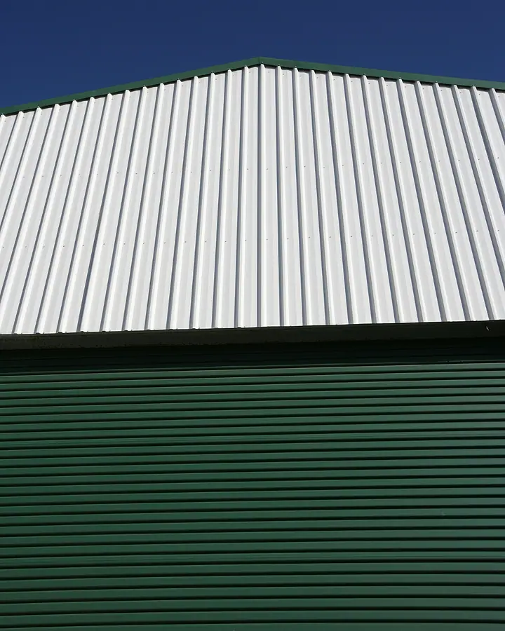 Fachada de galpão metálico verde com telhado de zinco sob o céu azul