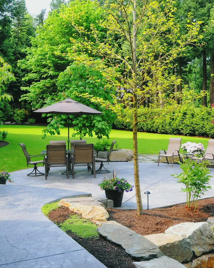 Jardim com gramado, canteiros floridos, caminho de pedra e mesa com guarda-sol