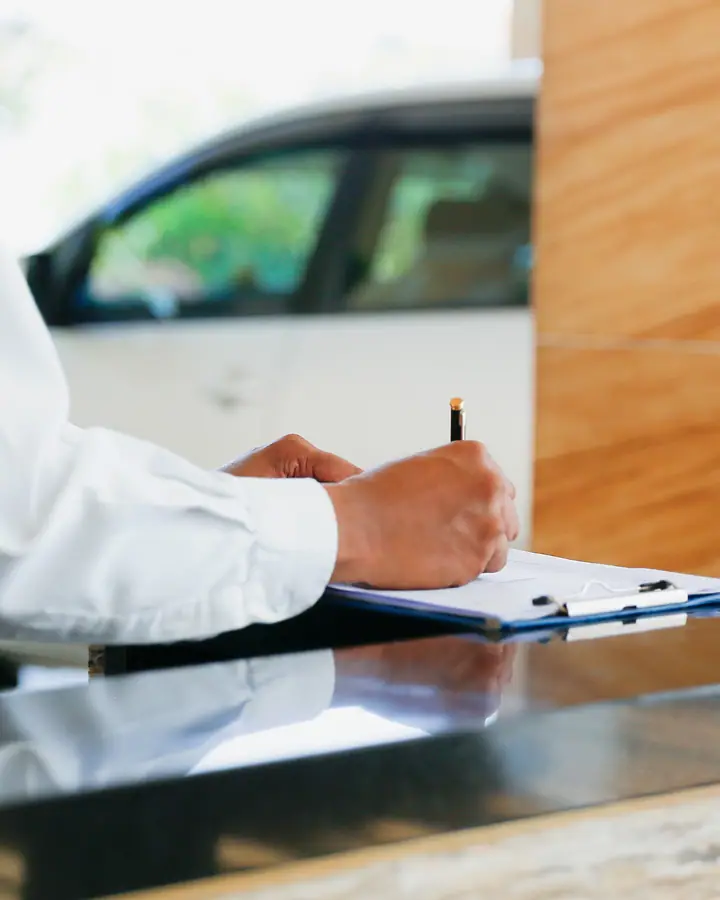 Profissional de camisa branca anotando o registro de entrada num balcão, com um carro ao fundo